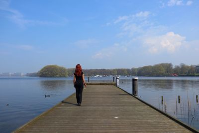 Rear view of woman standing on pier over lake against sky