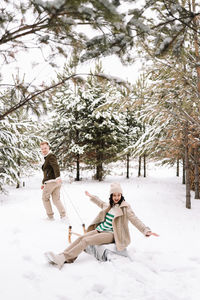 A man and a woman in love have fun and ride a sleigh in the forest among the trees in nature