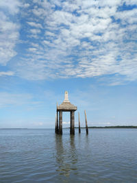 Gazebo in sea against cloudy sky