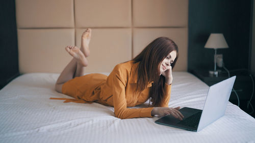 Young woman using laptop while lying on bed at home