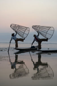 Men fishing in lake at sunset