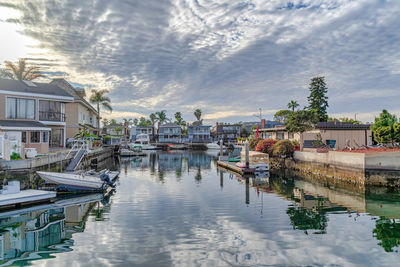 Boats moored in canal by buildings against sky