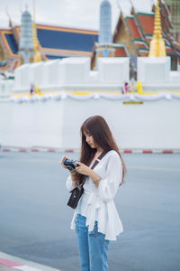 Young woman using mobile phone standing by road