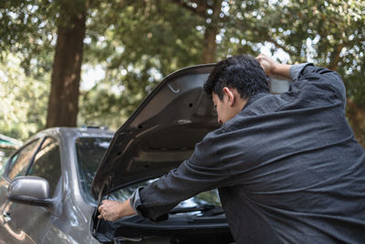 Rear view of man repairing car outdoors