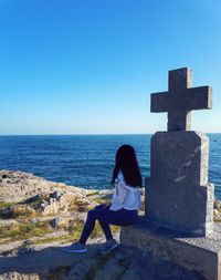 Woman sitting on beach against clear blue sky