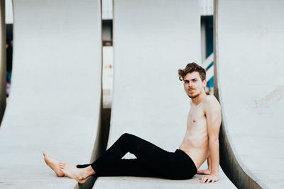Portrait of shirtless man sitting on built structure