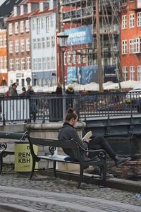 Woman sitting on seat in city against buildings