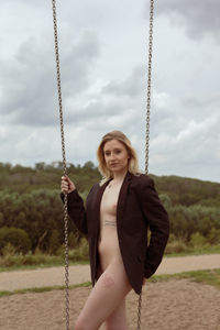 Young woman smiling while standing on swing against sky