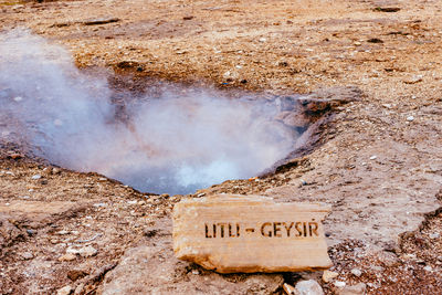 Close-up of text on rock by geyser against sky