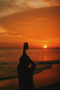 Silhouette man standing by sea against orange sky