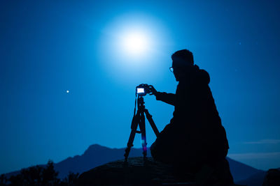 Silhouette of man photographing against blue sky