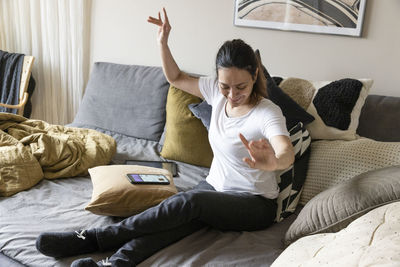 Carefree young woman with paraplegia dancing while sitting on sofa at home