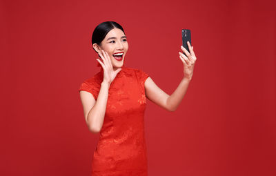 Smiling young woman using mobile phone against red wall