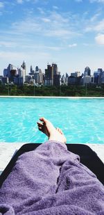 Low section of person with purple towel relaxing by swimming pool in city during sunny day