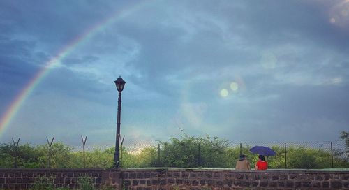 Rear view of people on street against rainbow in sky