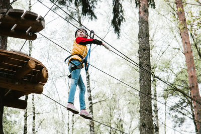 Low angle view of girl zip lining in forest