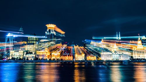 River against blurred motion of illuminated the bund amidst towers in city