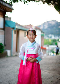 Portrait of girl standing on road against houses