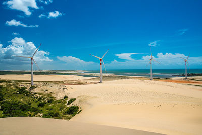 Wind turbines on beach against blue sky