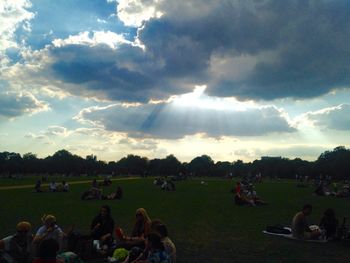 People on grassy field against cloudy sky