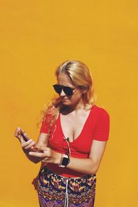 Woman using mobile phone while standing against orange wall during sunny day