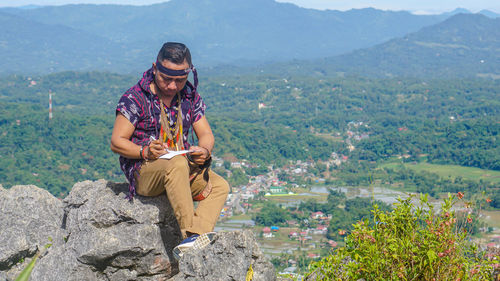 Rear view of man sitting on rock