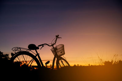 Silhouette of bicycle on field against sky during sunset