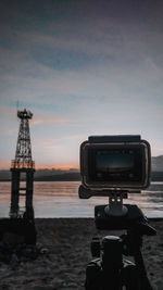 Camera on beach against sky during sunset