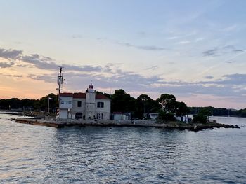 Buildings by sea against sky during sunset