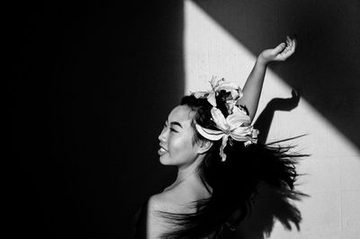 Happy young woman wearing flower against wall