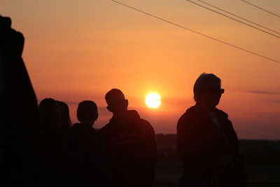 Silhouette people against orange sky during sunset