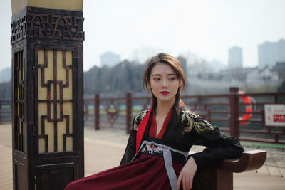 Thoughtful woman wearing traditional clothing while sitting on seat in city