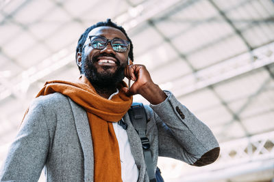 Smiling man talking on mobile phone while standing against ceiling