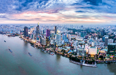 Aerial view of cityscape by river against cloudy sky during sunset