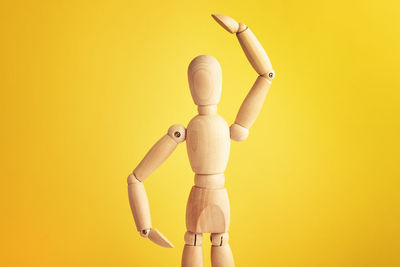 Wooden doll with gesture on yellow background. mannequin shows gesture. figure of wooden human