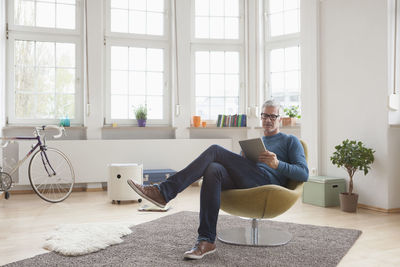 Mature man at home sitting in chair using digital tablet