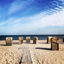 Wooden chairs on beach against sky