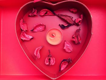 High angle view of rose petals with tea light candle in heart shape container