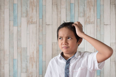 Thoughtful boy looking away while standing against wall