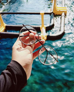 Cropped hand holding eyeglasses against sea