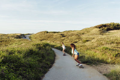 Back view of anonymous multiethnic women skaters riding skate board down the road in countryside