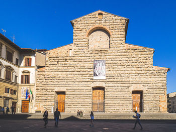 People walking outside historic building against clear blue sky