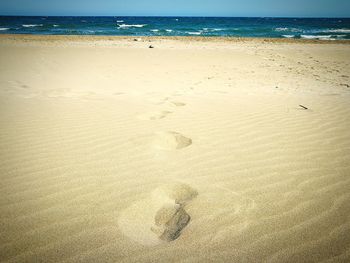 Footprints on sand at beach against sky