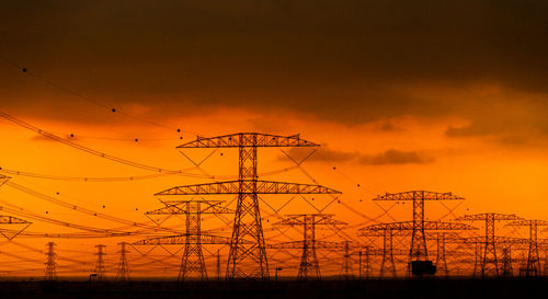 Low angle view of silhouette electricity pylon against sky during sunset