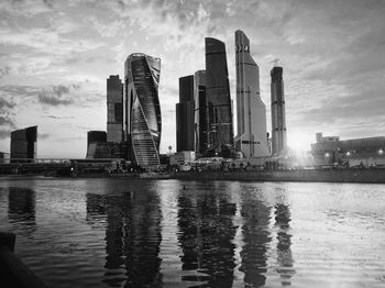 Modern buildings by river against sky in city