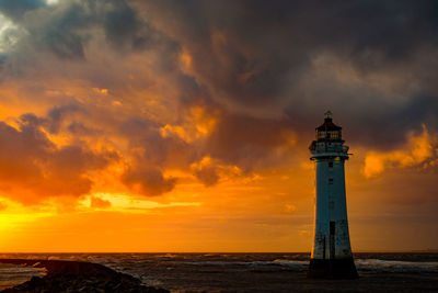 Lighthouse by sea against sky during sunset