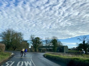 People riding bicycle on road in city against sky