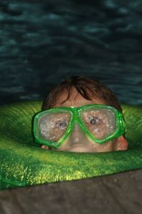 Close-up portrait of teenage boy wearing swimming goggles in pool