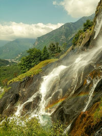 Scenic view of waterfall and rainbow against sky