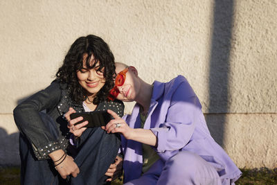 Smiling female friends or gay couple taking selfie with cell phone